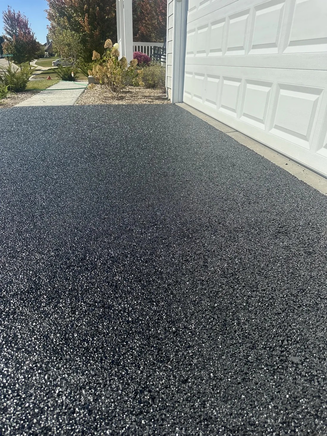 Close-up of freshly sealed black asphalt beside a garage